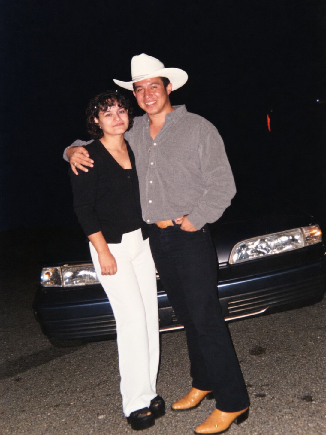 My dad and my mom standing in front of a car at night